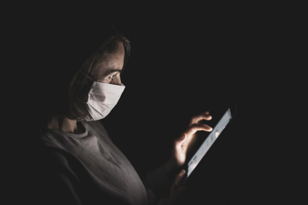 Photo of woman in face mask scrolling on her phone.